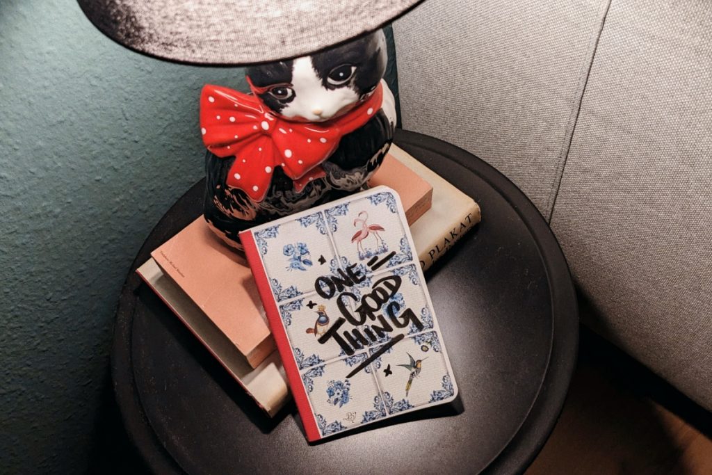 Notizbuch auf einem schwarzen Beistelltisch mit Büchern und einer Lampe in Form einer Porzellankatze