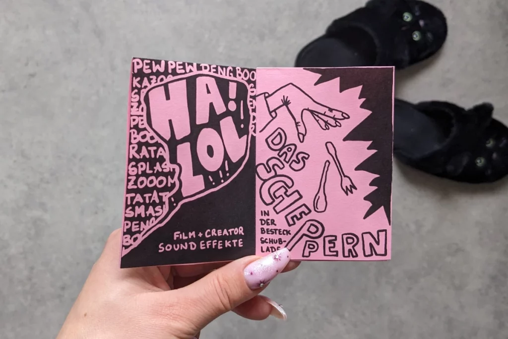 Geöffnete Doppelseite: Zeichnung große Sprechblase mit "Ha! LOL!" - Film und Creator Sound Effekte. Zeichnung Hand, die Besteck fallen lässt: Das Scheppern in der Besteckschublade.