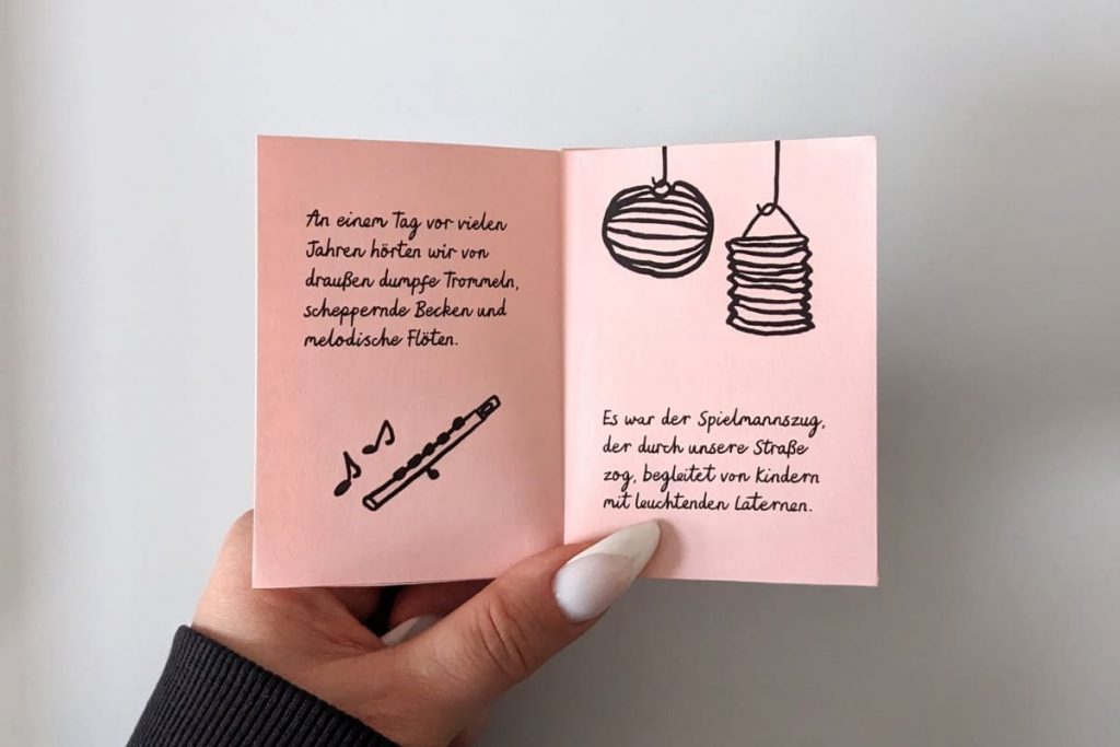 Hand hält geöffnetes Zine. Kindlich illustrierte Querflöte mit tanzenden Noten und zwei Papier-Laternen. Alle Texte im Beitrag.