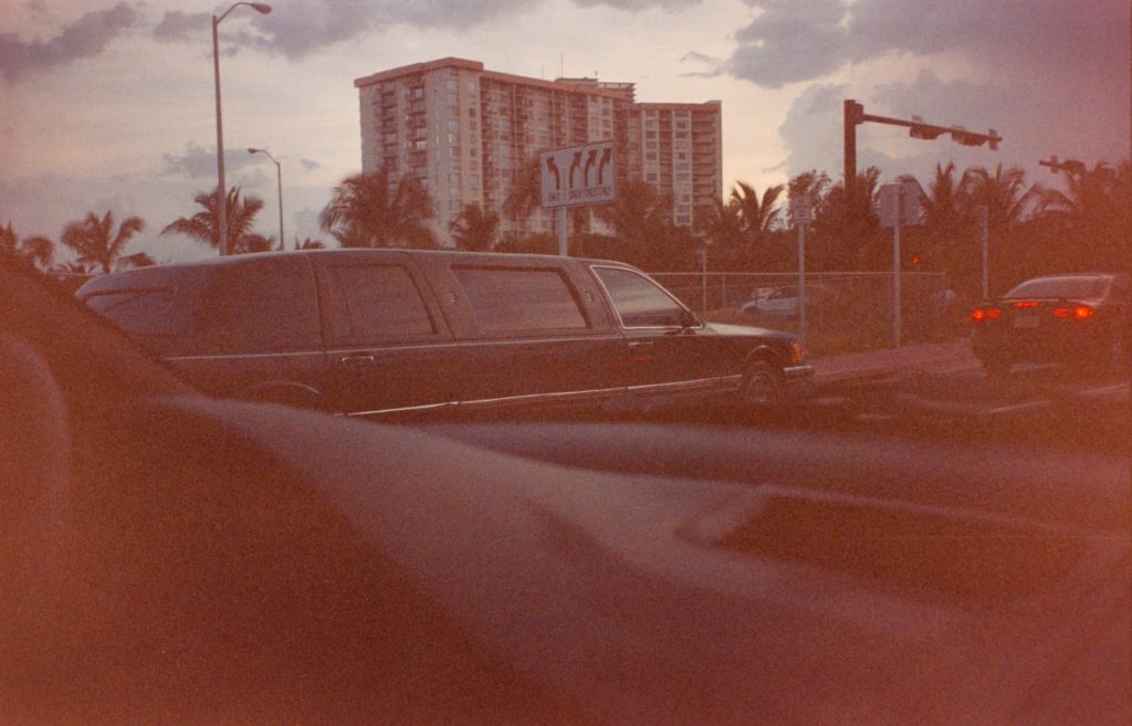 Lange schwarze Limousine vor Hochhäusern und Palmen in der Abenddämmerung, fotografiert aus dem Auto.