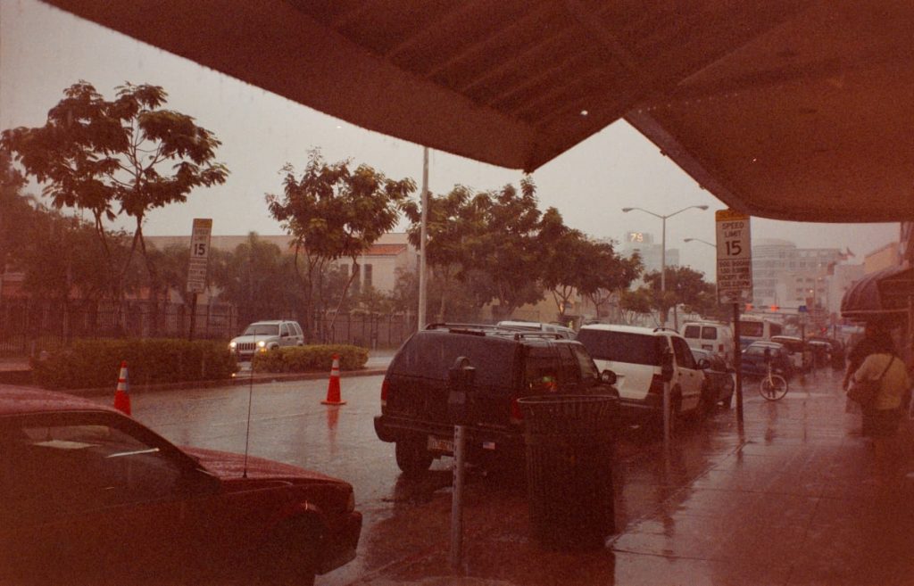 Starker Regen in einer Straße mit parkenden Autos und Schildern für Geschwindigkeitsbegrenzung.