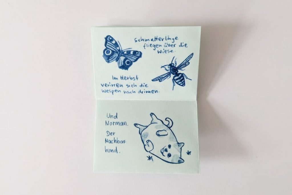 Offenes Zine mit blauen Zeichnungen eines Schmetterlings, einer Wespe und einem dicken Hund, der fröhlich auf dem Rücken liegt sowie handgeschriebenem Text