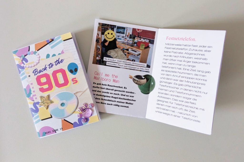Zwei Mini-Zines „Back to the 90s“. Buntes Cover mit CD-Rom, Alien-Kopf und Stickern. Auf der Innenseite ein Foto eines Kinderzimmers mit Röhrenmonitor, Holzmöbeln und Texten über das „Festnetztelefon“ und Rauchen.