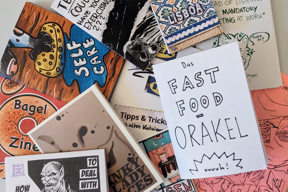 Eine bunte Sammlung handgemachter Mini-Zines mit verschiedenen Titeln und Illustrationen ungeordnet auf einem Tisch