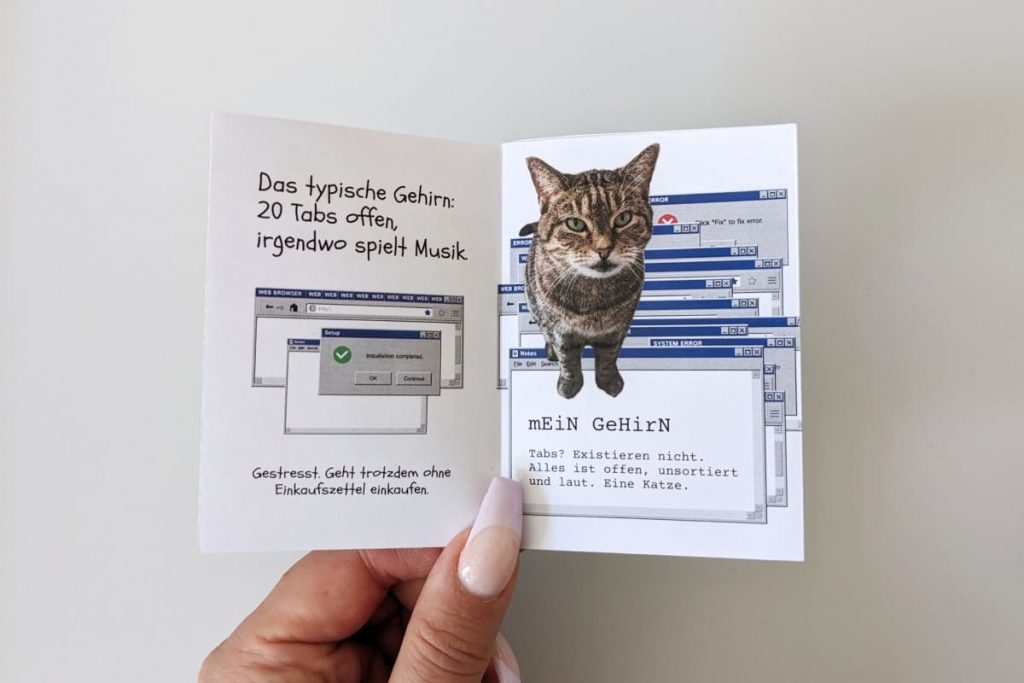 Doppelseite vergleicht „Das typische Gehirn“ (20 offene Tabs) mit „mein Gehirn“: ein Chaos aus übereinandergestapelten Windows-Fenstern, auf denen eine Katze thront. Der Text beschreibt das eigene Gehirn als unsortiert, laut, und mit einer Katze.