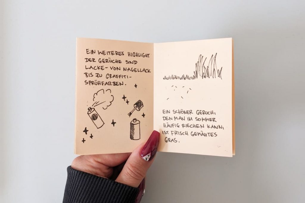 Offene Seite eines Zines mit Texten und einfachen Strichzeichnungen über Nagellack, Graffiti-Sprühfarben und frisch gemähtem Gras.