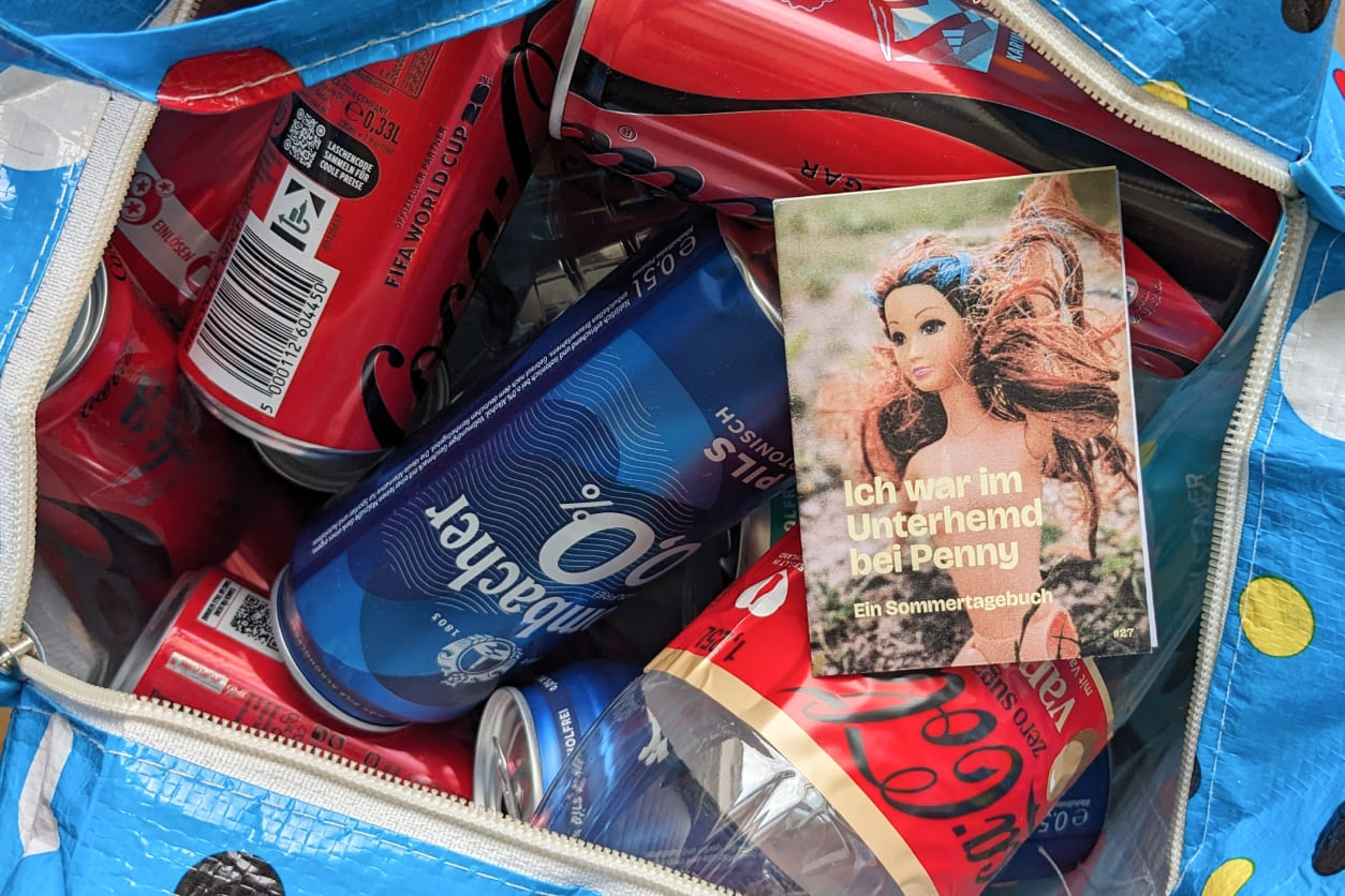 Blaue Einkaufstasche mit Punkten, gefüllt mit Pfandflaschen und einem Mini-Zine: "Ich war im Unterhemd bei Penny"