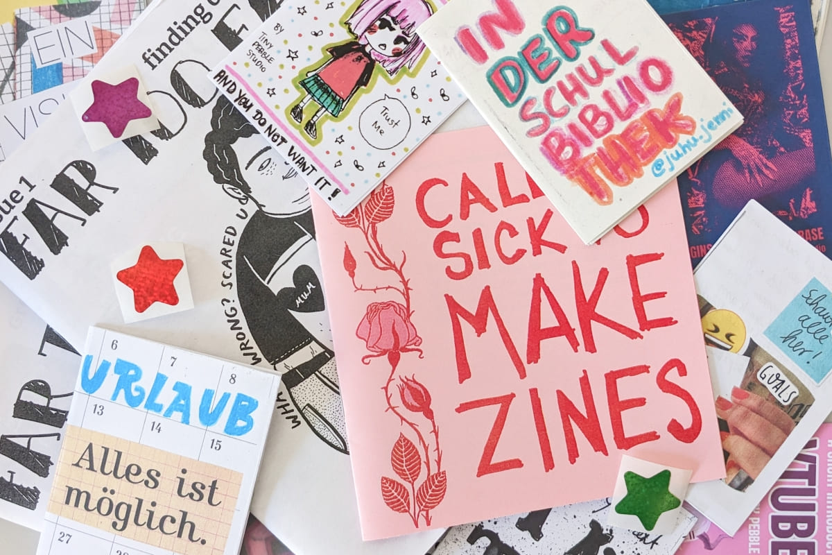 Viele verschiedenen handgemachte Zines liegen wild auf einem Haufen, dazwischen Sterne-Aufkleber.