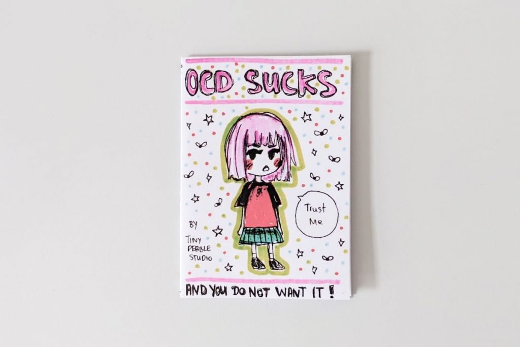 Cover des Zines „OCD Sucks“ von Tiny Pebble Studio mit Zeichnung eines Mädchens mit rosa Haaren und vielen bunten Punkten.