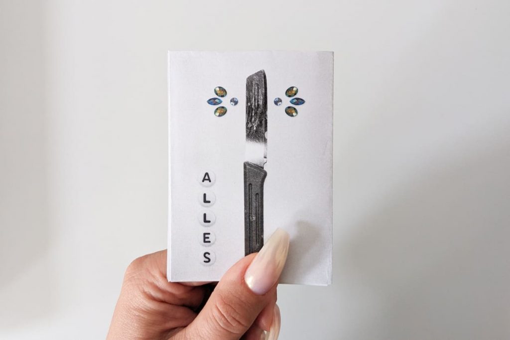 Rückseite mit freigestelltem Messer: Klinge in klassischer Form eines Brötchenmessers (gerade). Buchstabenperlen: ALLES.